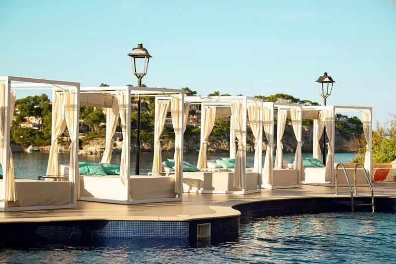 Des lits de repos blancs et beiges sont installés sur une plateforme en bois au bord de l'eau.
