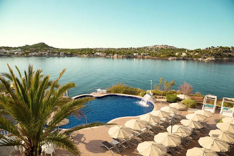 Vue sur une piscine et la mer depuis une terrasse ensoleillée.