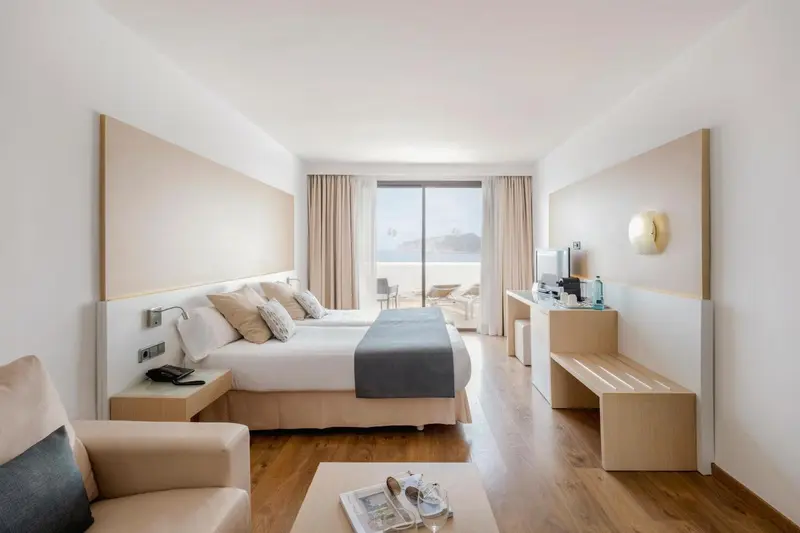 Chambre lumineuse avec un grand lit et un accès à une terrasse.