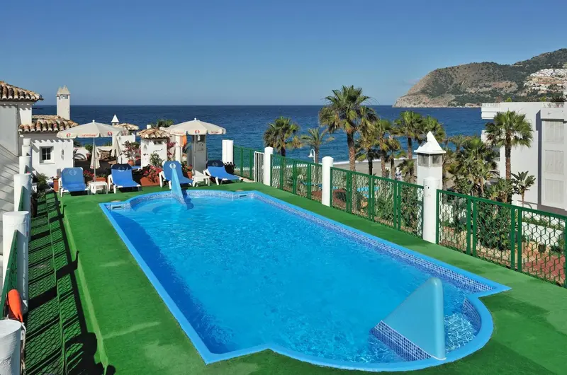 Une piscine rectangulaire turquoise avec une zone peu profonde pour enfants, entourée d'une terrasse en gazon synthétique.