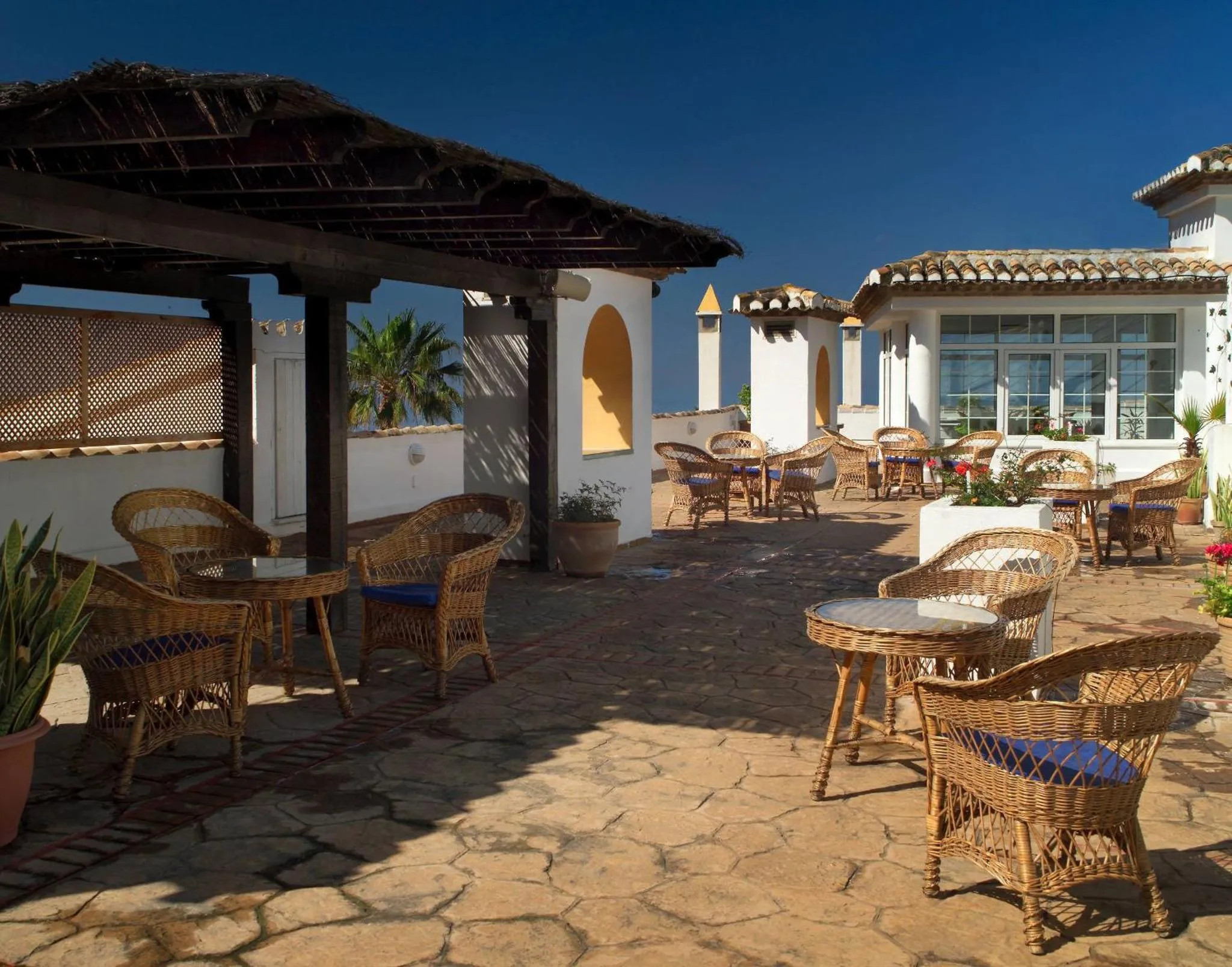 Terrasse ombragée avec mobilier en rotin et vue sur la mer.