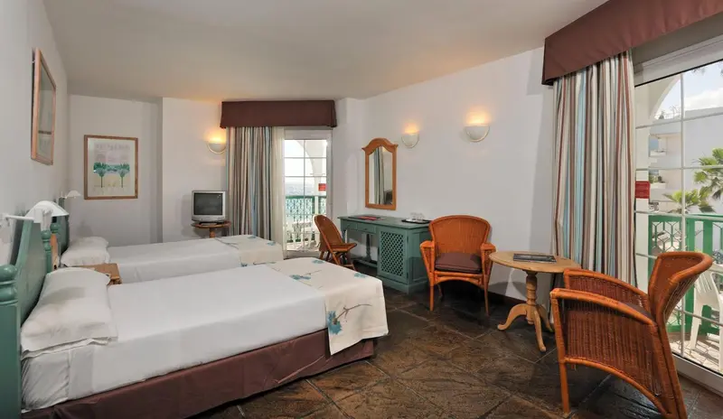 Une chambre lumineuse avec deux lits et un coin salon donnant sur une terrasse.