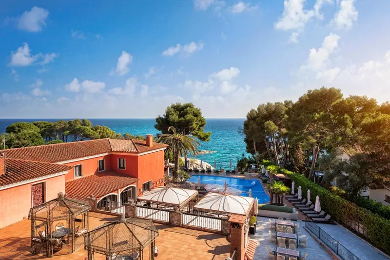 Vue aérienne d'un bâtiment aux toits rouges surplombant une piscine et la mer.