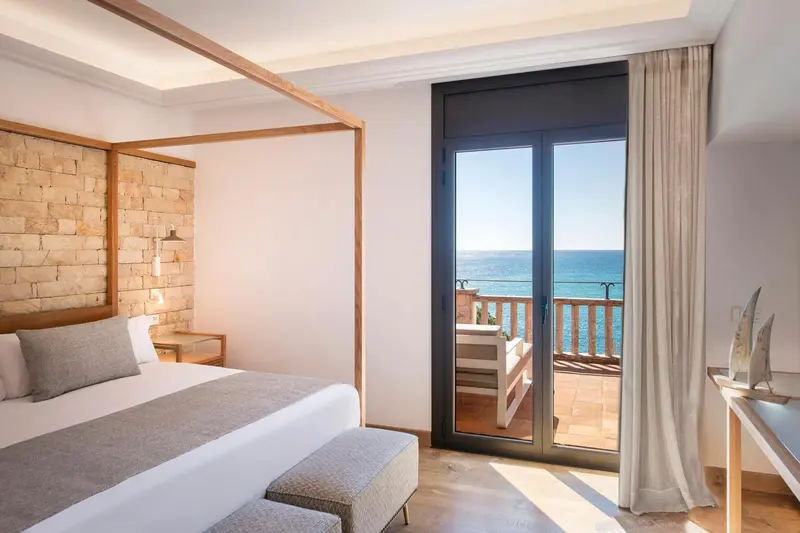 Une chambre lumineuse avec un grand lit et une vue sur la mer depuis un balcon.