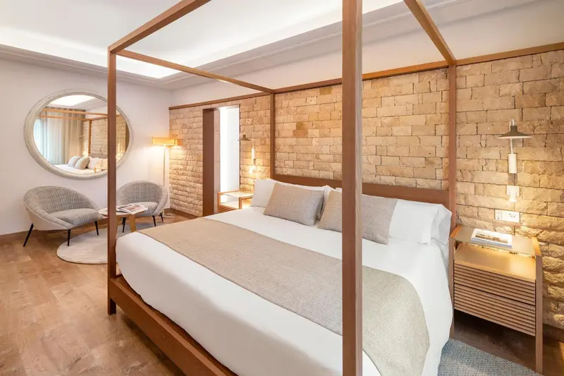 Une chambre lumineuse avec un lit à baldaquin et un mur en pierre.