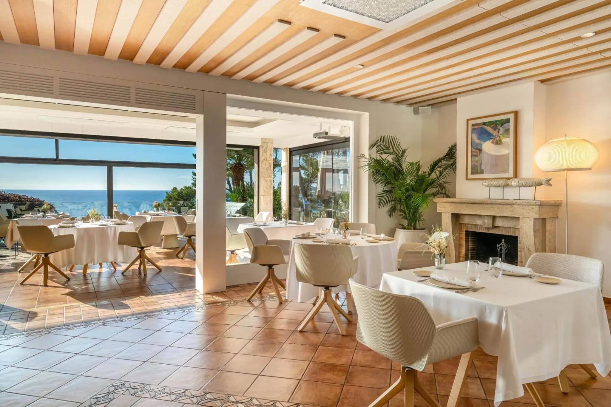 Une salle lumineuse avec des tables dressées face à une vue sur la mer.