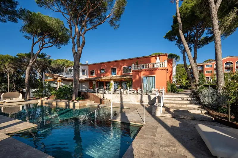 Bâtiment orange entouré de végétation et surplombant une piscine bleue.