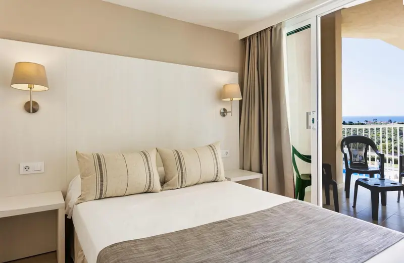 Une chambre lumineuse avec un grand lit et un balcon donnant sur la mer.