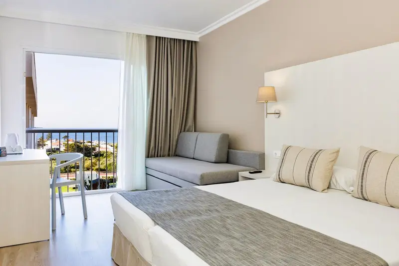 Une chambre lumineuse avec un lit et un canapé face à une baie vitrée.