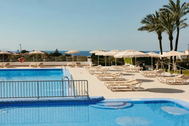 Transats et parasols bordent une piscine turquoise ensoleillée.