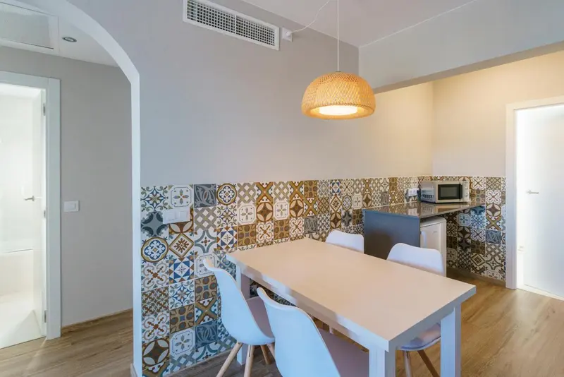 Une salle à manger lumineuse avec une table et des chaises devant un mur décoré de carreaux.