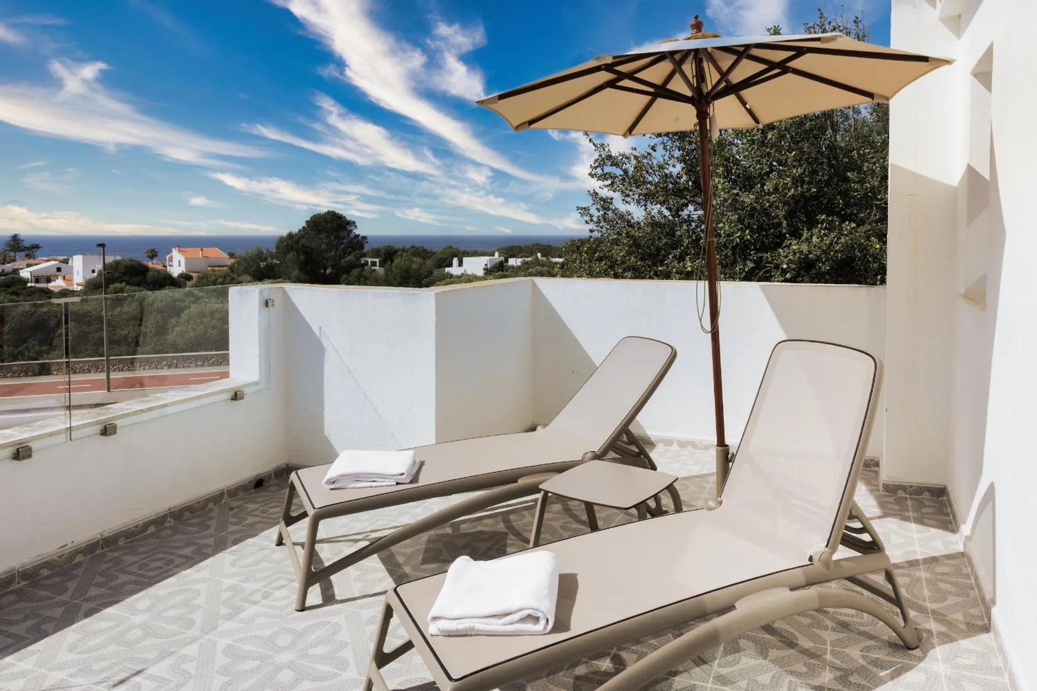 Deux transats blancs sur une terrasse ensoleillée avec vue sur la mer et les collines.