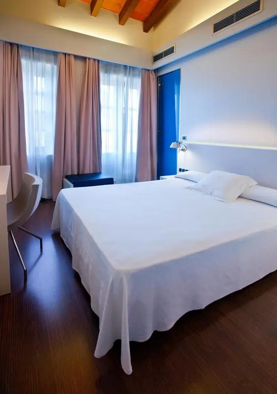Une chambre lumineuse avec un grand lit et des rideaux roses.