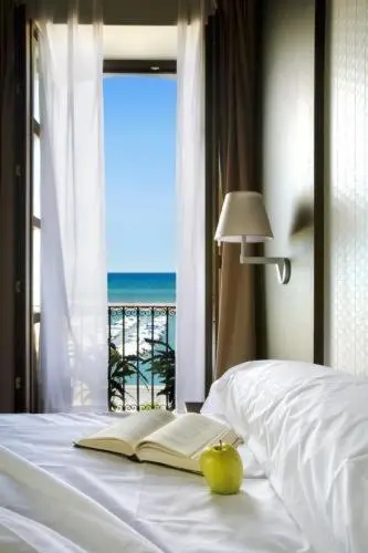 Un lit avec un livre ouvert et une pomme verte, devant une fenêtre donnant sur la mer.