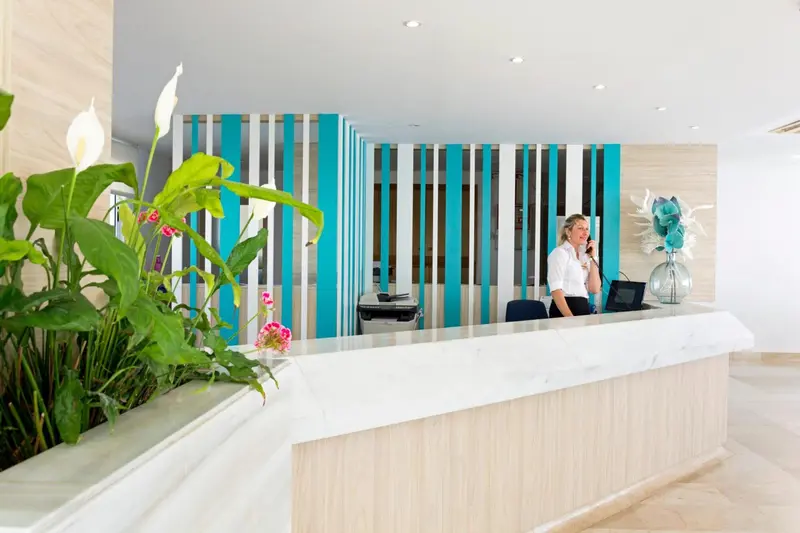 Un comptoir d'accueil moderne avec une employée au téléphone et une décoration florale.