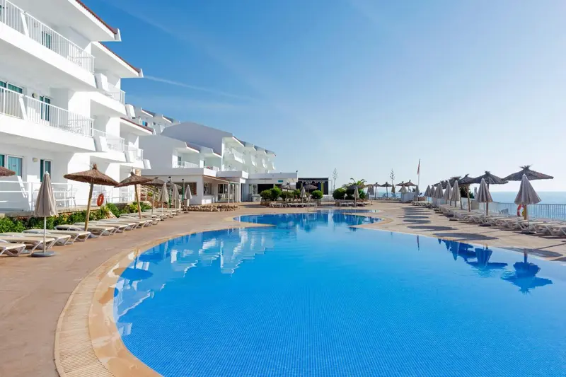 Piscine bleue bordée de transats devant un bâtiment blanc.