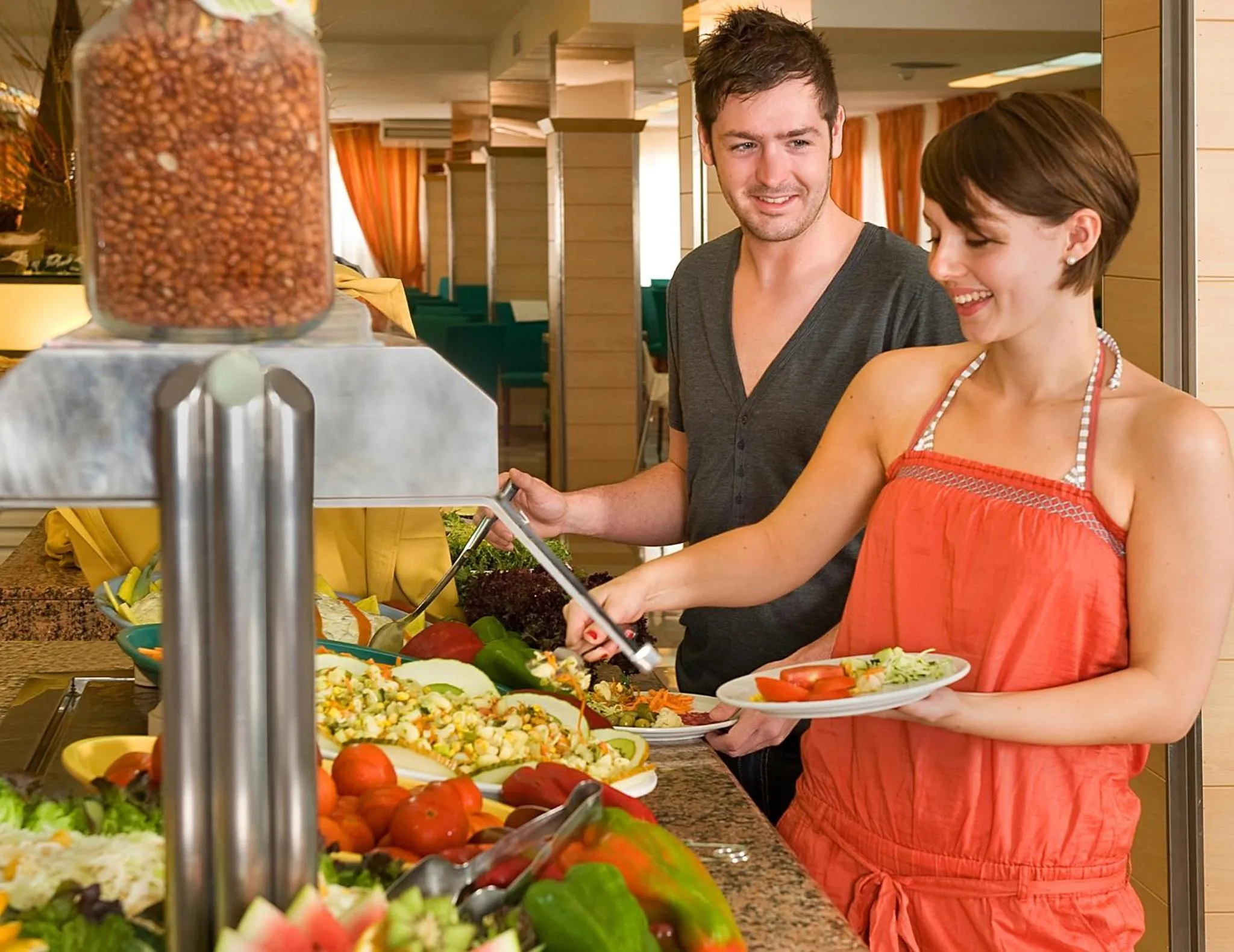 Un couple se sert à un buffet de salades dans une salle lumineuse.