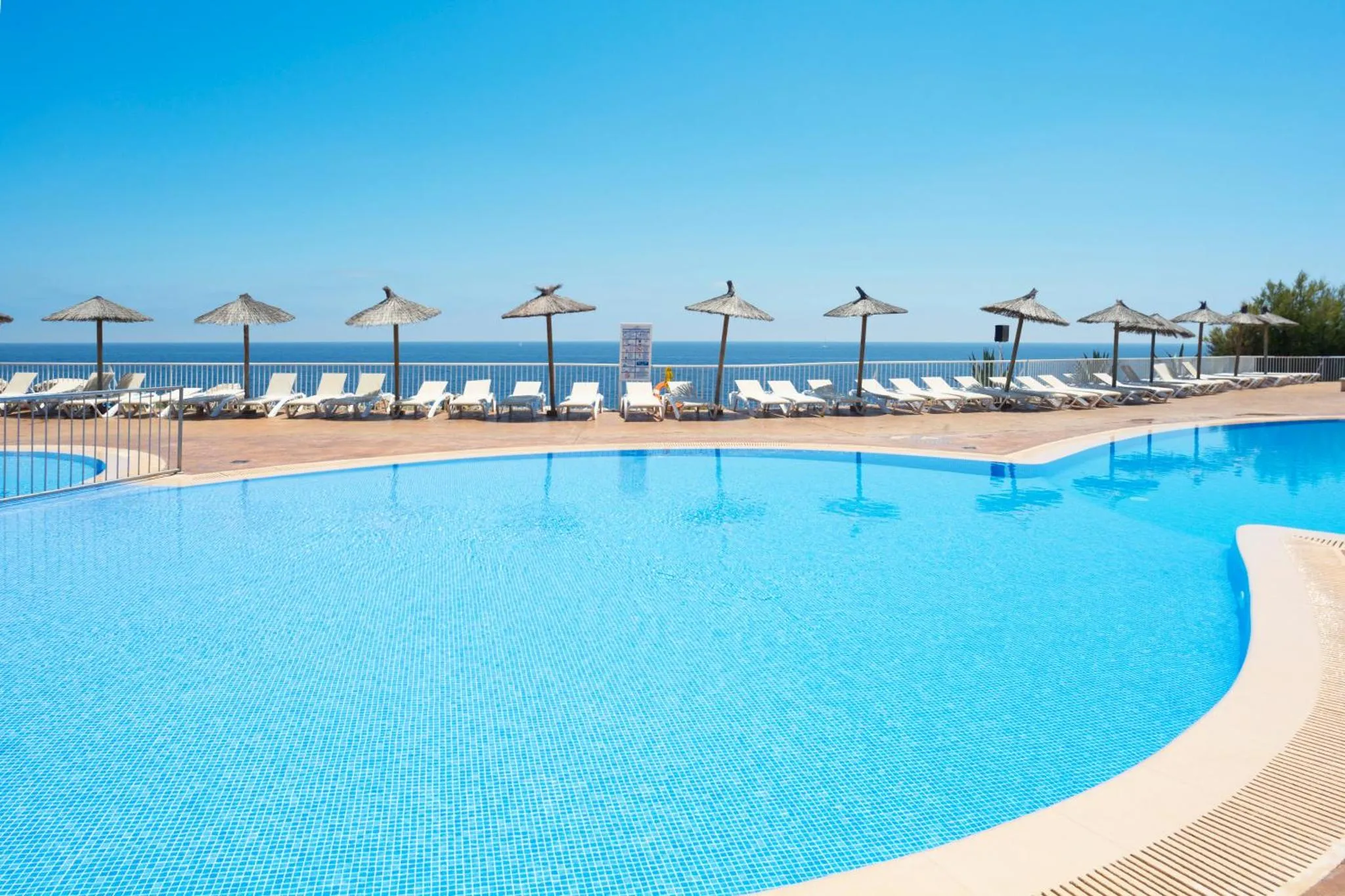 Transats alignés au bord d'une piscine turquoise sous des parasols.