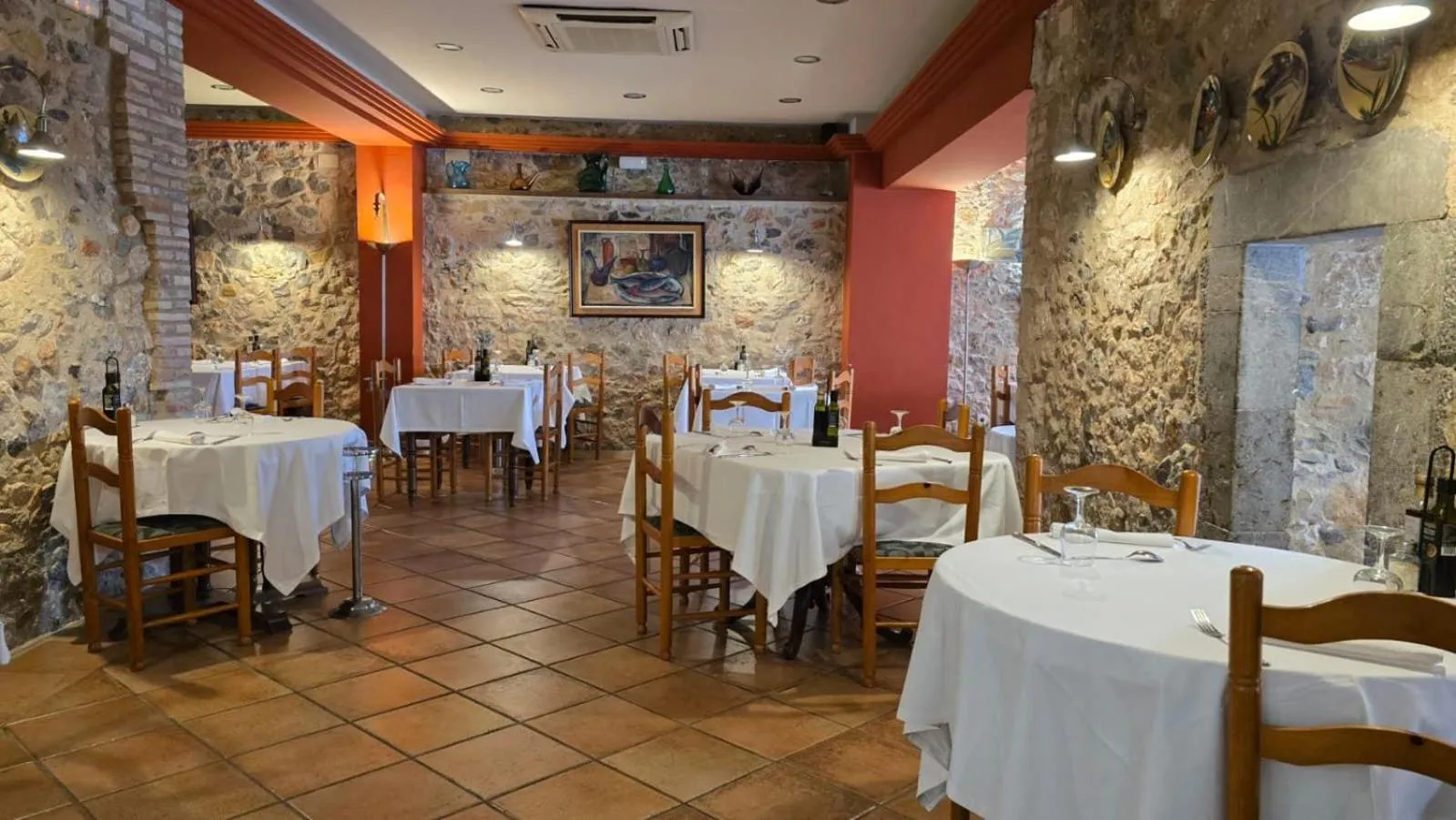Une salle de restaurant avec des tables nappées et un décor en pierre.