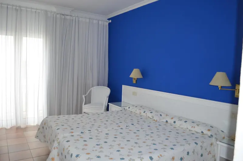 Une chambre lumineuse avec un lit recouvert d'une courtepointe fleurie et deux lampes de chevet.