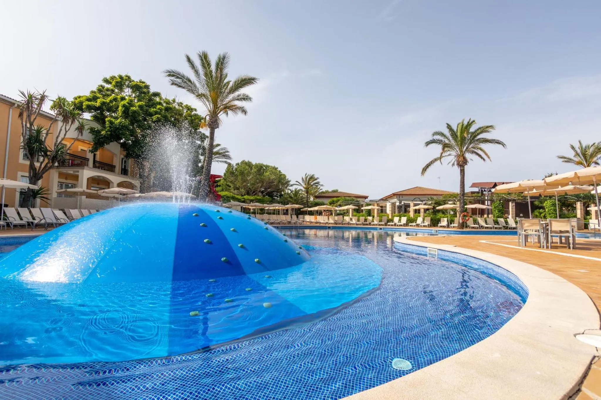 Piscine avec fontaine et transats sous des palmiers.