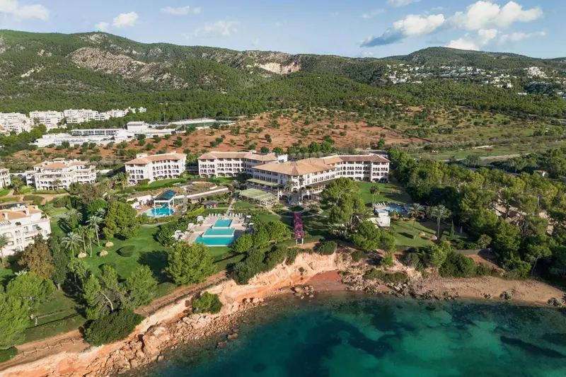 Vue aérienne d'un complexe hôtelier en bord de mer avec piscine et végétation luxuriante.