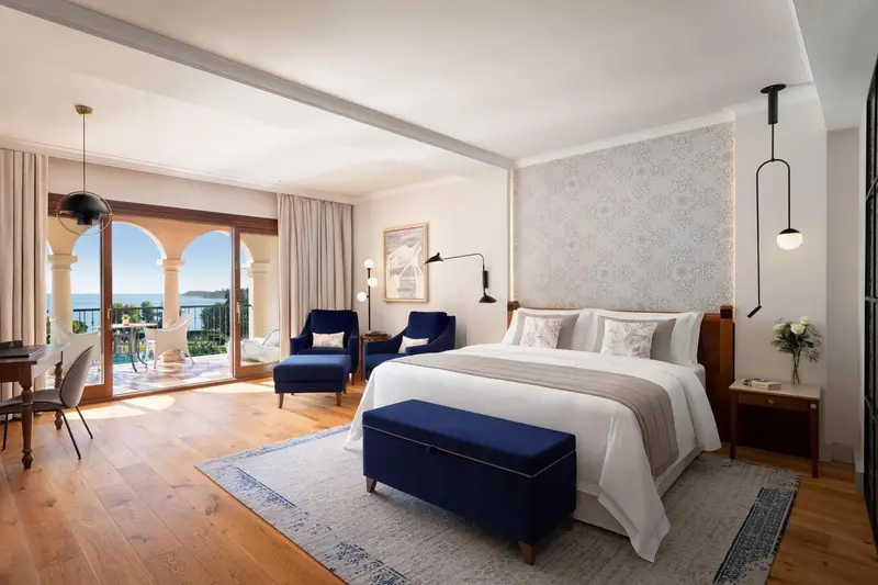 Chambre lumineuse avec un grand lit et un accès à une terrasse avec vue sur la mer.
