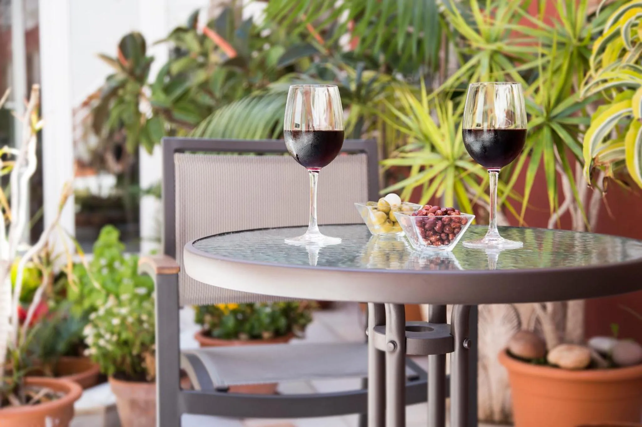 Deux verres de vin rouge et une corbeille de fruits sur une table ronde en extérieur.
