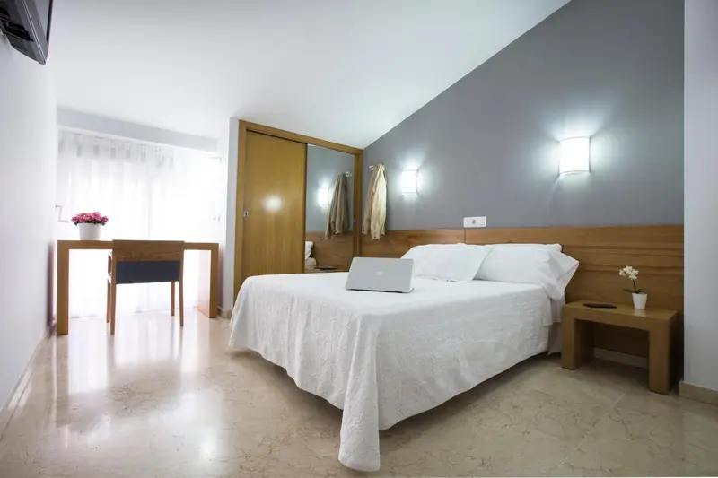 Une chambre lumineuse avec un lit blanc et un bureau en bois.