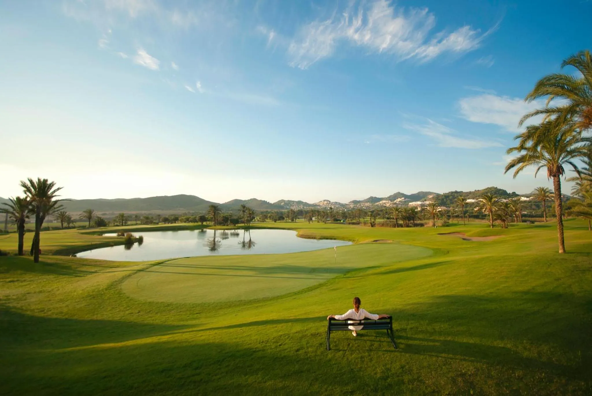 Un homme se repose sur un banc au bord d'un terrain de golf verdoyant.