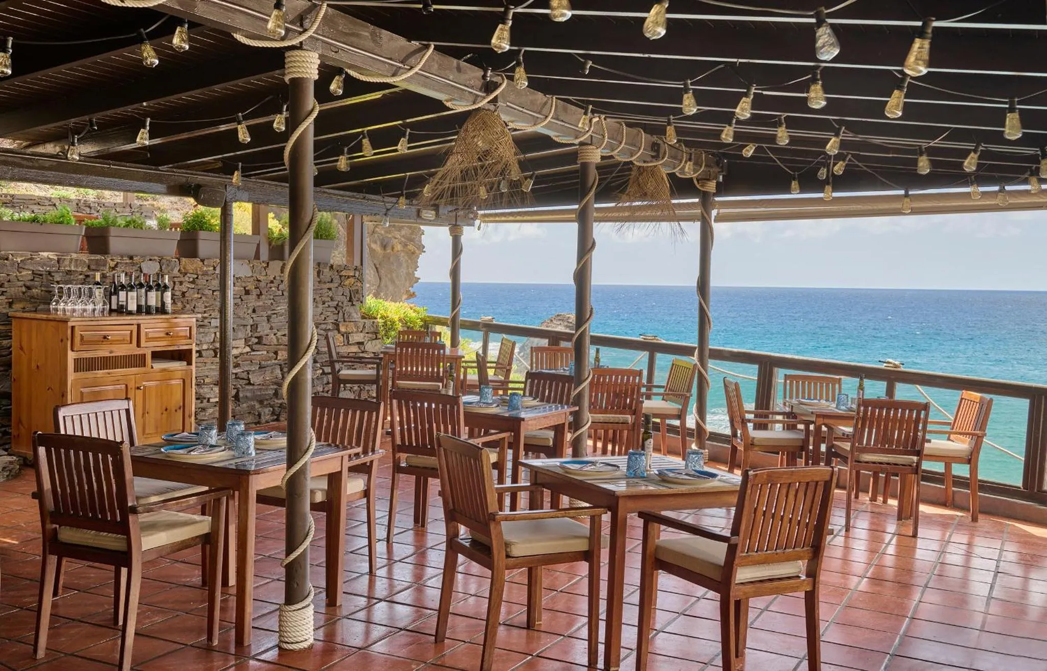 Terrasse ombragée avec tables et chaises donnant sur la mer.