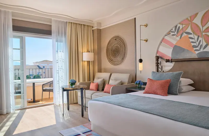 Une chambre lumineuse avec un lit et un coin salon donnant sur un balcon.
