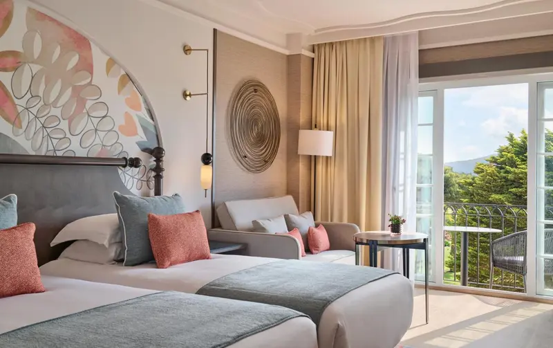 Chambre lumineuse avec un grand lit et un coin salon donnant sur une vue verdoyante.