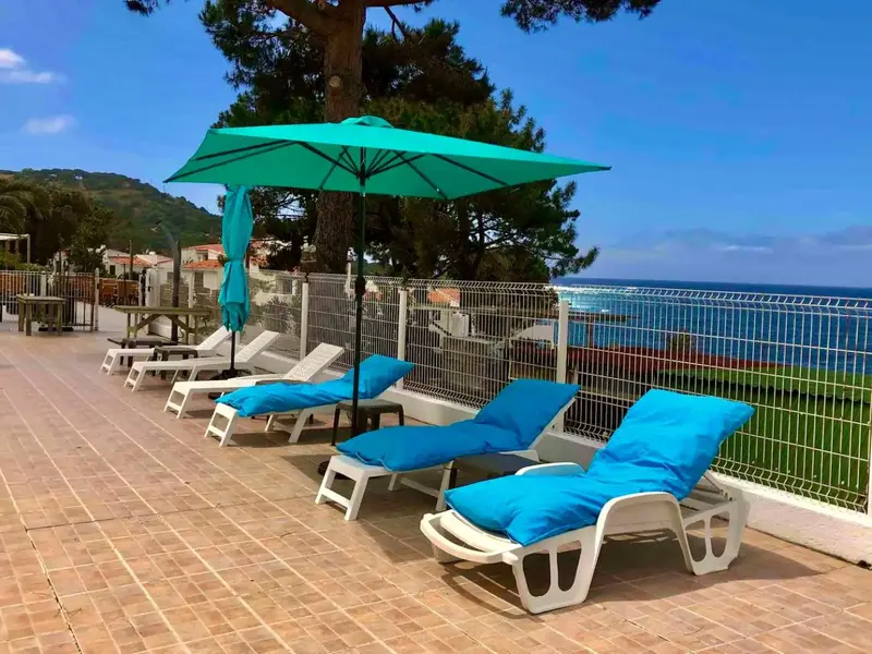 Transats bleus sous des parasols verts sur une terrasse ensoleillée avec vue sur la mer.