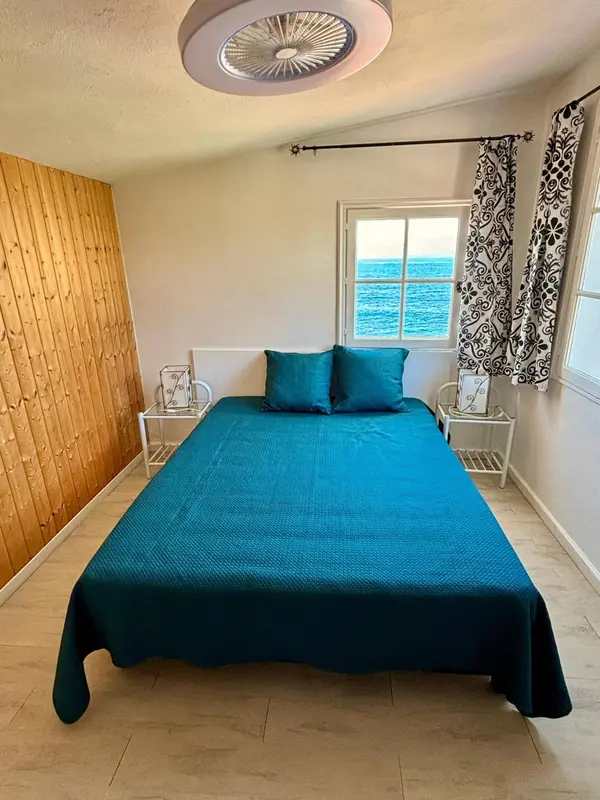 Une chambre avec un lit recouvert d'une couverture turquoise et une vue sur la mer.