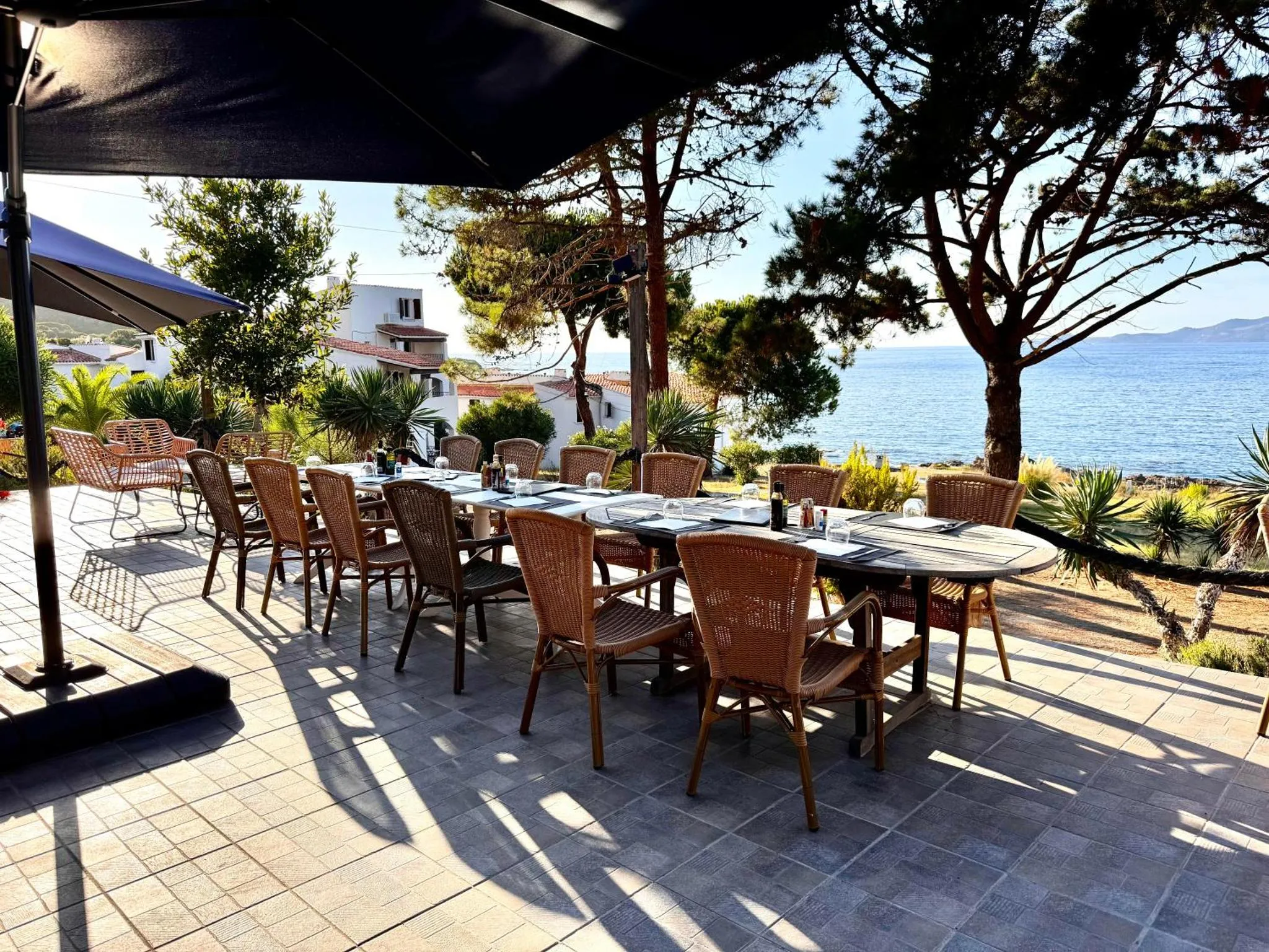 Une longue table est dressée sur une terrasse ombragée avec vue sur la mer.
