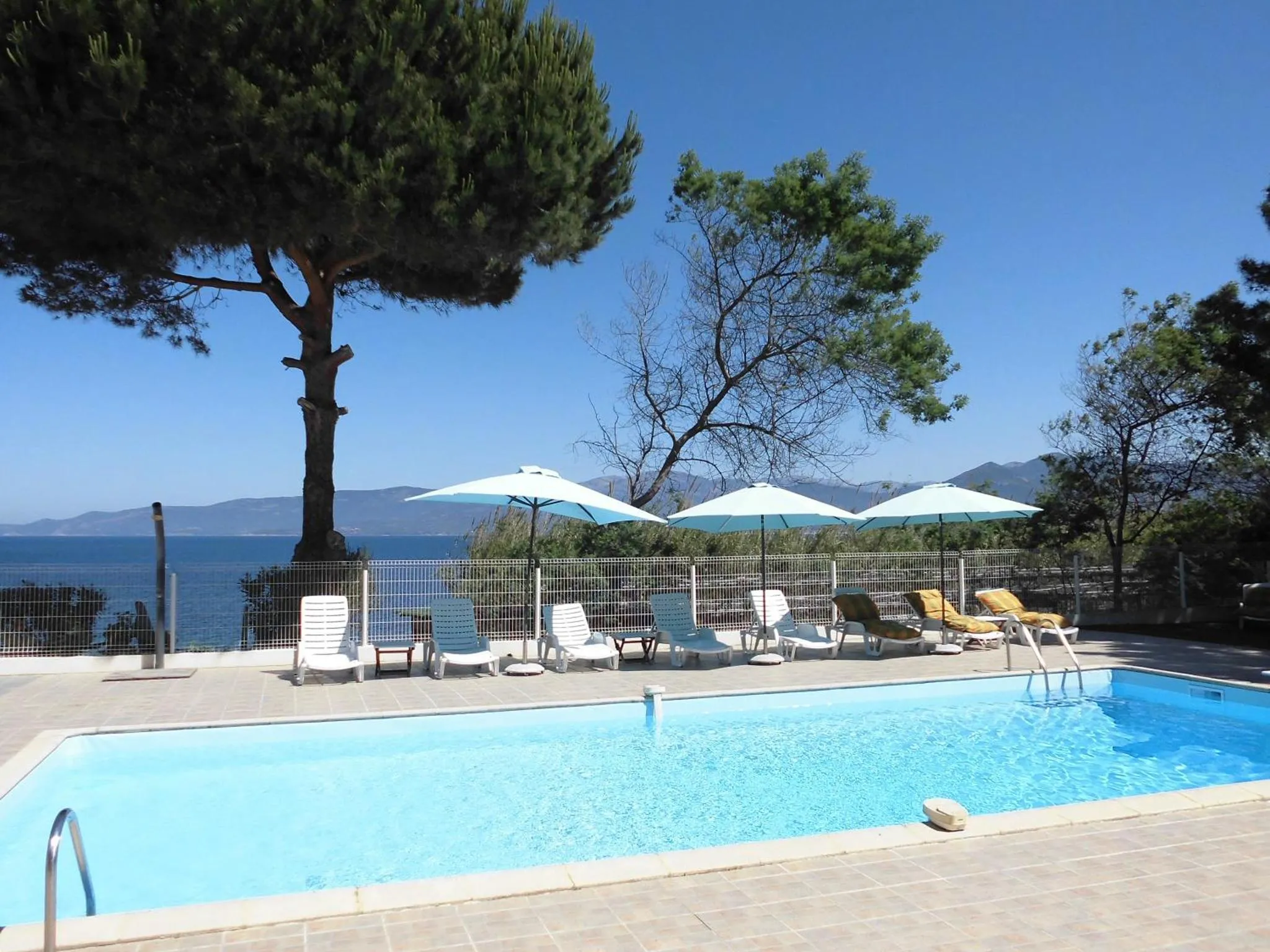 Transats et parasols bordent une piscine en extérieur avec vue sur la mer.