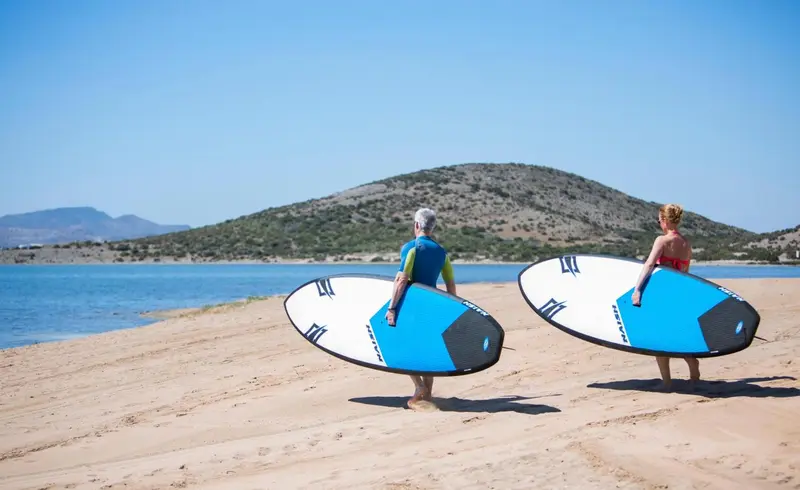 Deux personnes se promènent sur une plage en portant des planches de surf.
