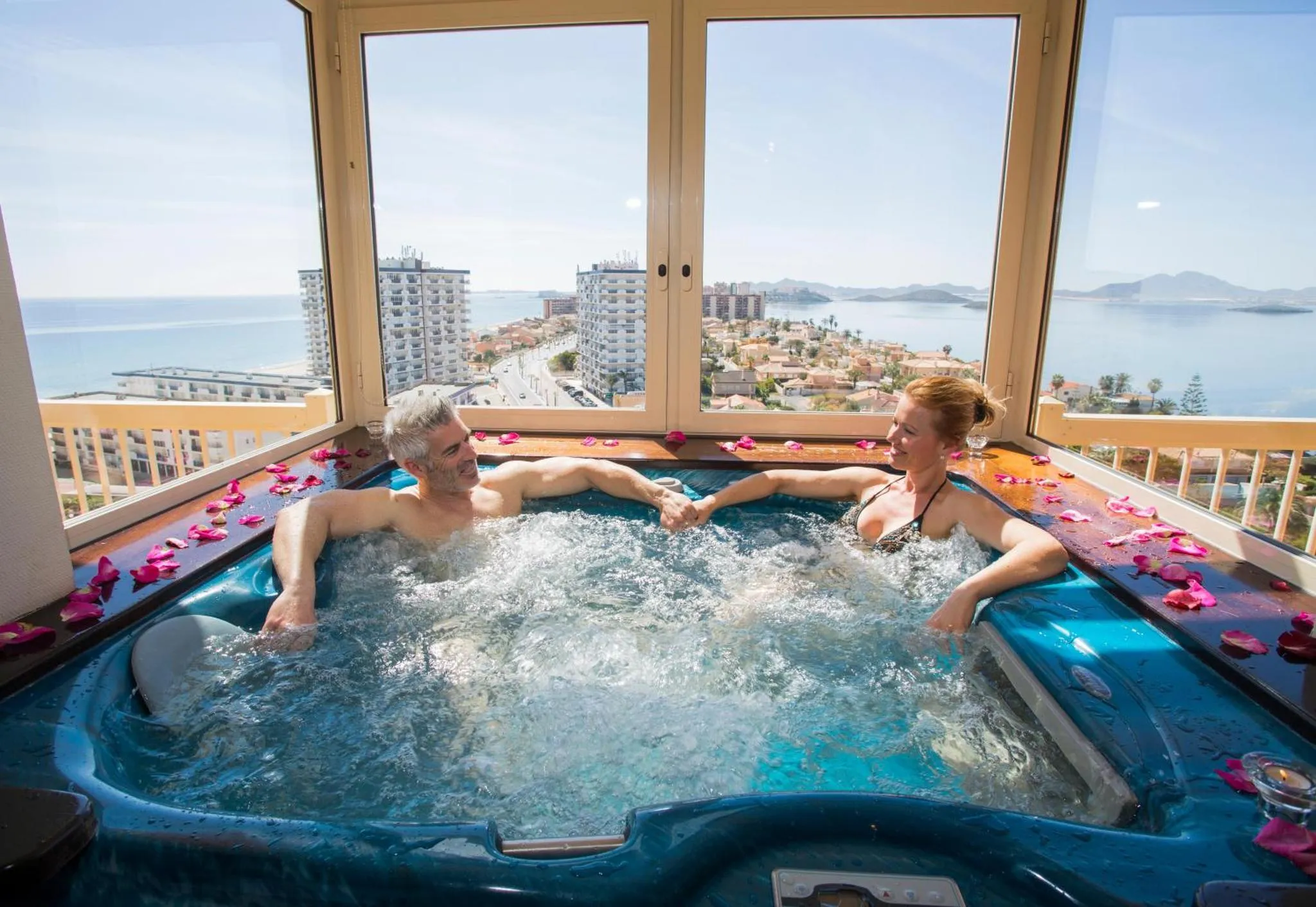 Un couple se détend dans un jacuzzi avec vue sur la mer et la ville.