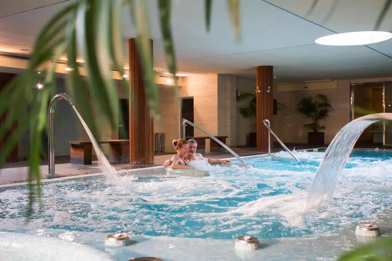 Des personnes se détendent dans un bassin intérieur avec des jets d'eau.