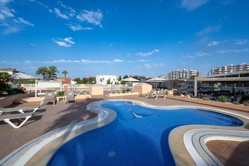 Piscine extérieure avec transats et parasols sous un ciel bleu nuageux.