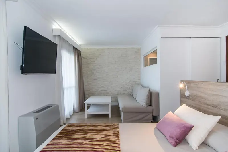 Une chambre lumineuse avec un lit et un canapé face à un téléviseur mural.