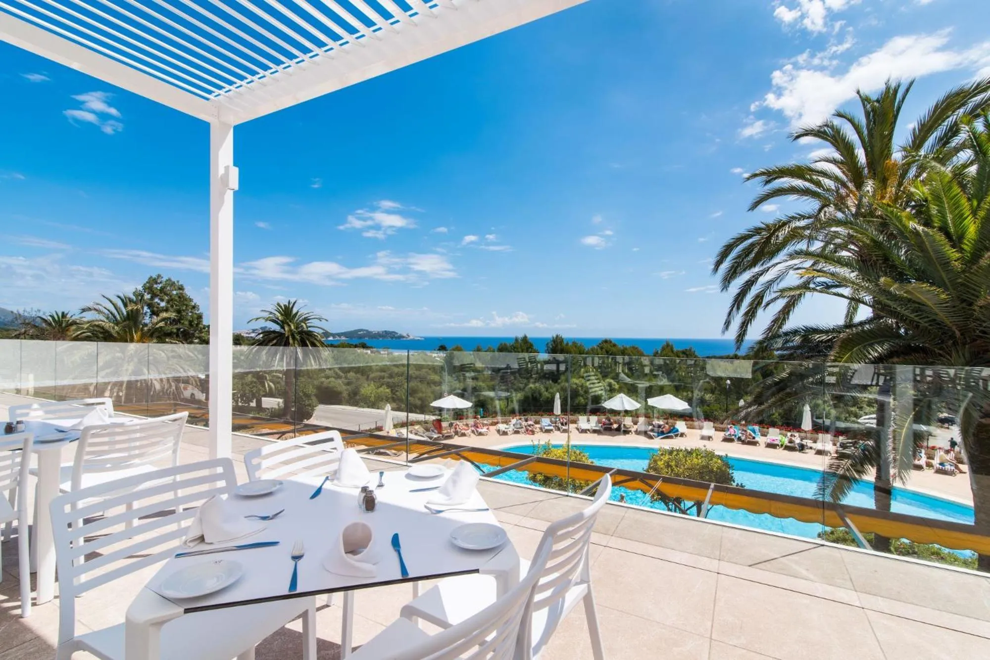 Terrasse avec tables dressées donnant sur une piscine et la mer.