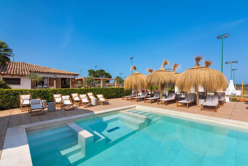 Transats et parasols de paille disposés autour d'une piscine ensoleillée.