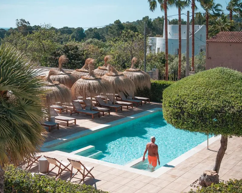 Une piscine rectangulaire bordée de chaises longues et de parasols en chaume.