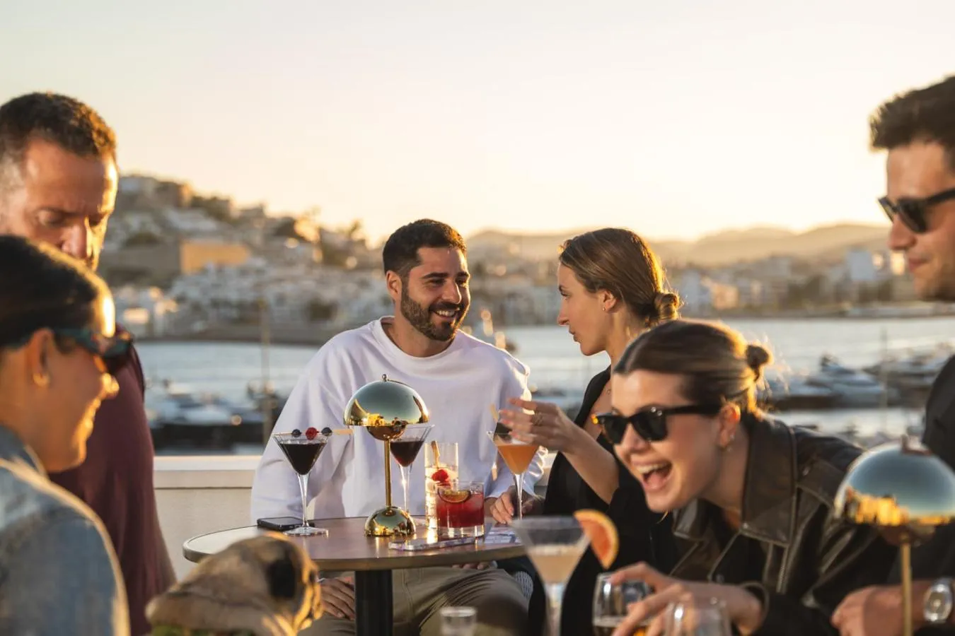 Un groupe de personnes profite de cocktails sur une terrasse ensoleillée avec vue sur la mer.