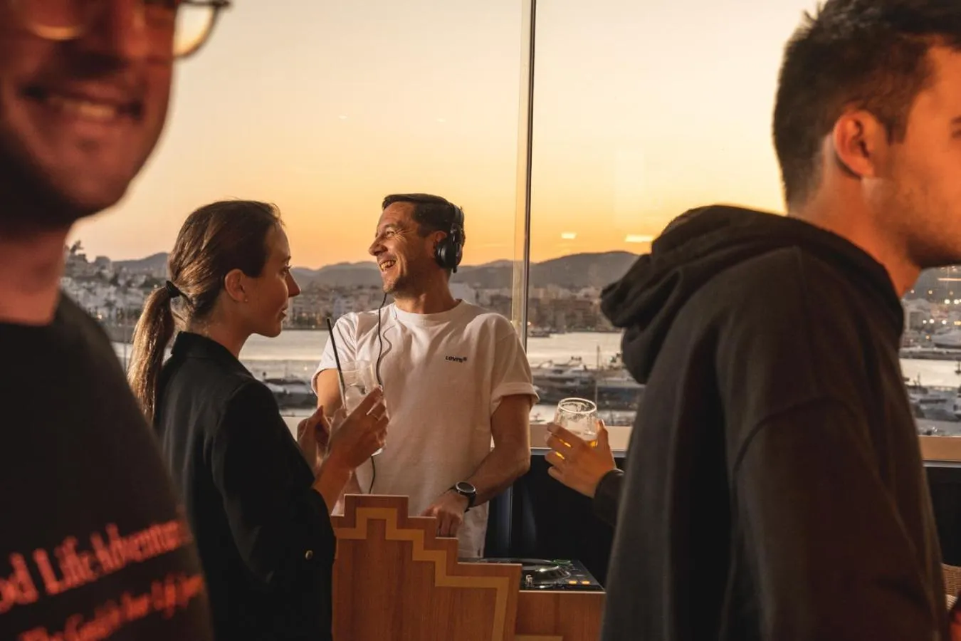 Des personnes discutent sur une terrasse avec vue sur la mer et la ville.
