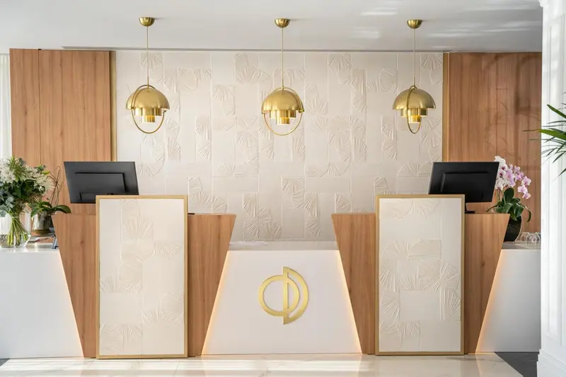 Un comptoir d'accueil moderne avec un mur décoratif en bois et des luminaires dorés.