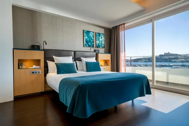 Chambre lumineuse avec un grand lit et une vue sur la mer.