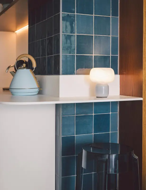 Une bouilloire et une lampe sur une étagère carrelée.